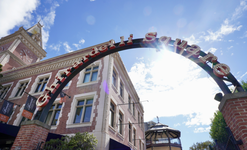 A low-angle shot of a brick building with a prominent archway reading 'Grand Hotel' in front of a blue sky with clouds.